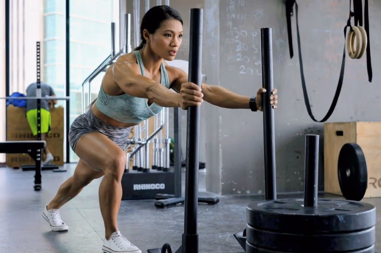 Athletic woman in workout attire pushing a weighted sled in a gym.