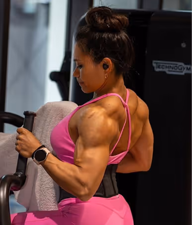 Muscular woman in a pink workout outfit using gym equipment for back exercises.