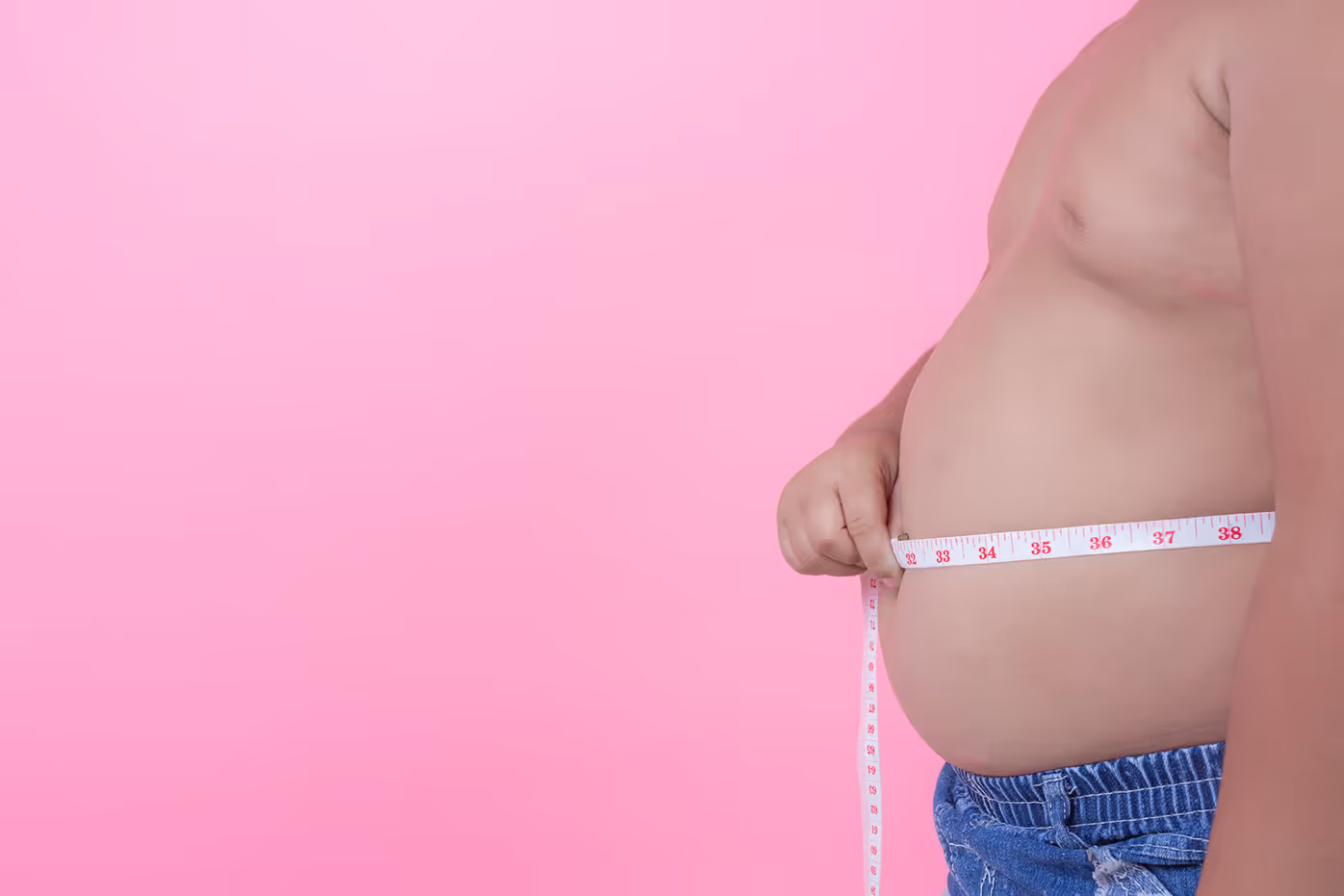 Overweight man measuring his waist with a tape measure against a pink background.